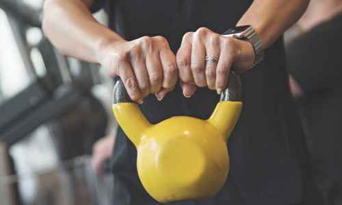Händer som håller i en gul kettle bell