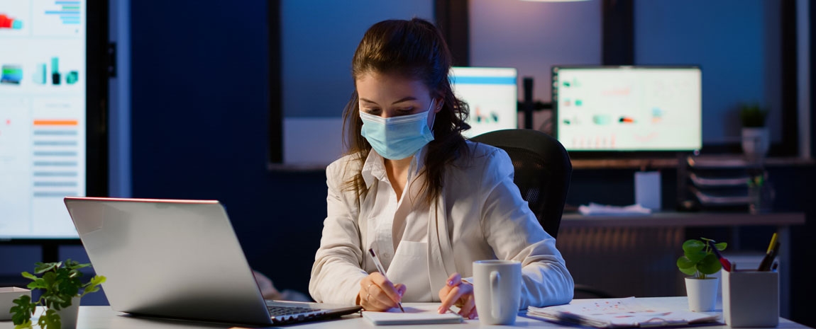 Kvinna med ansiktsmask vid skrivbord på kontor