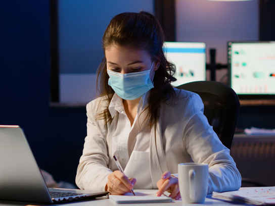 Kvinna med ansiktsmask vid skrivbord på kontor