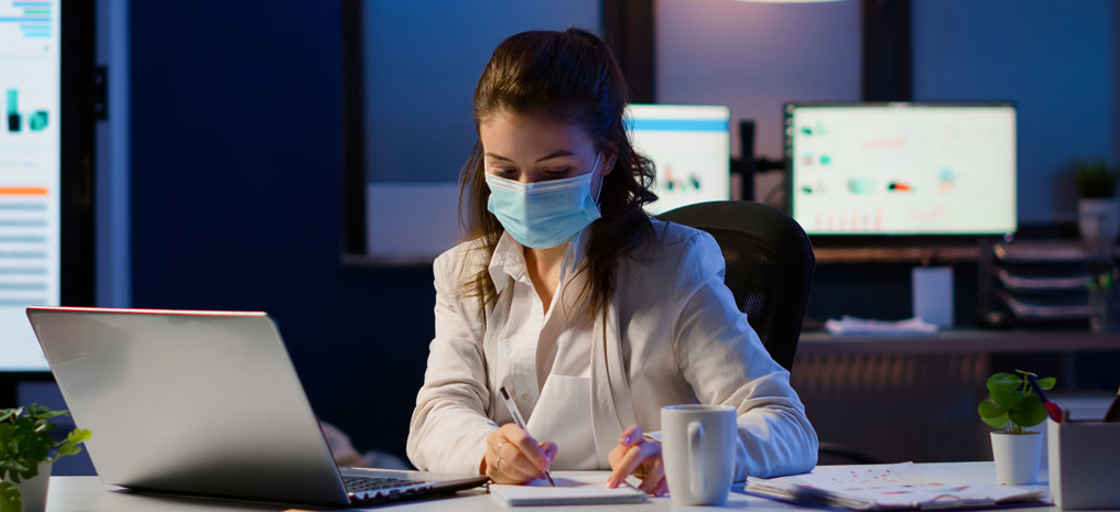 Kvinna med ansiktsmask vid skrivbord på kontor