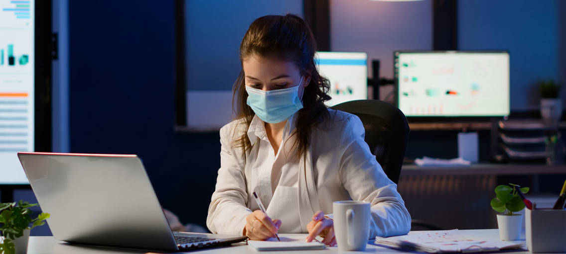 Kvinna med ansiktsmask vid skrivbord på kontor
