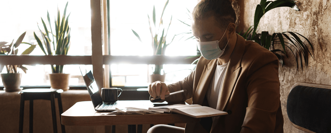 Man i skyddsmask sitter på café med laptop och jobbar