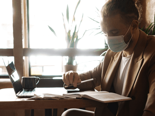 Man i skyddsmask sitter på café med laptop och jobbar
