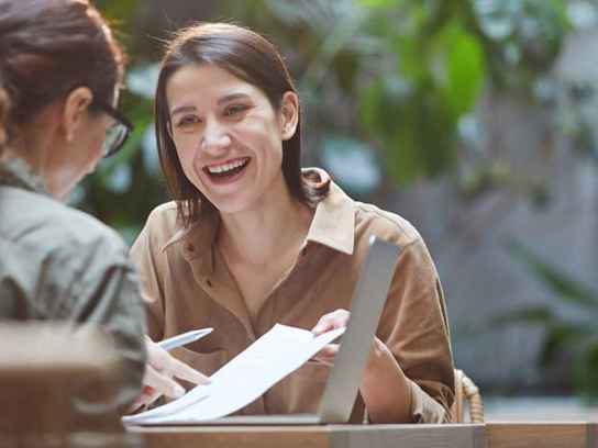 Två kvinnor samtalar vid ett bord med en laptop
