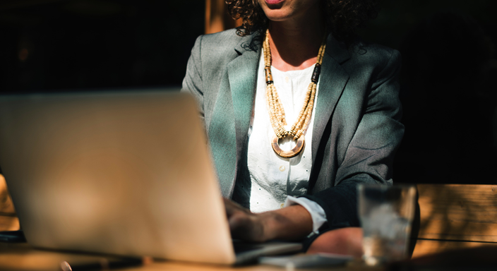 Jakkupukuinen nainen istuu kannettavan tietokoneen ääressä kädet tietokoneen näppäimistöllä