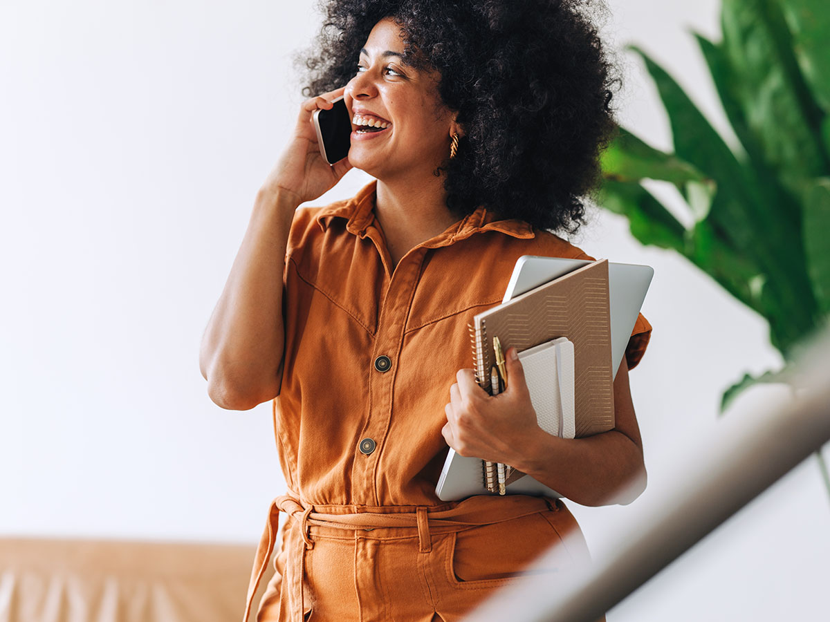 Vrouw met oranje top en schriften belt mobiel om zzp factoring aan te vragen 