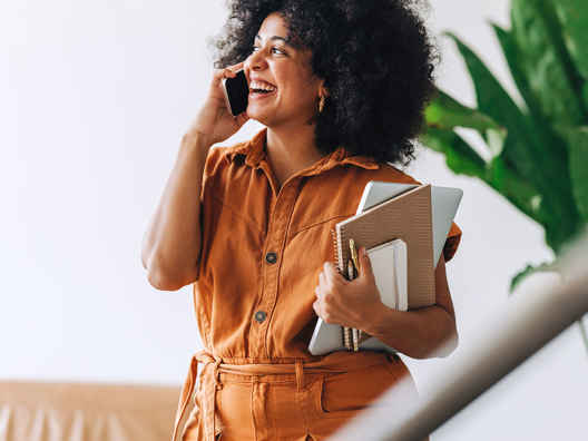 Vrouw met oranje top en schriften belt mobiel om zzp factoring aan te vragen 