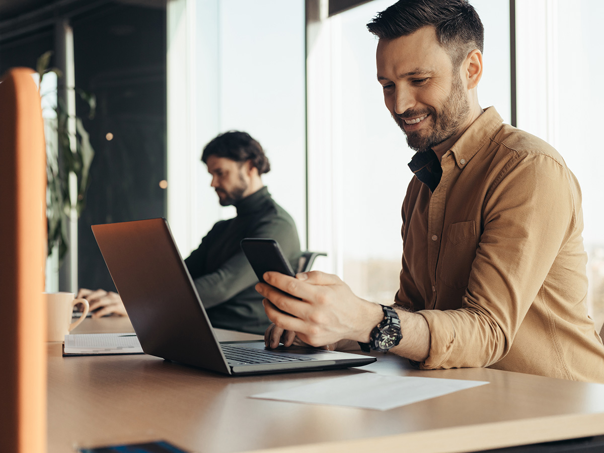 Mannen typen op laptop achter bureau op kantoor met telefoon om factuur direct betaald te krijgen