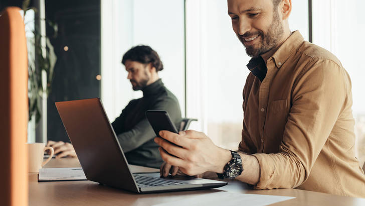 Mannen typen op laptop achter bureau op kantoor met telefoon om factuur direct betaald te krijgen
