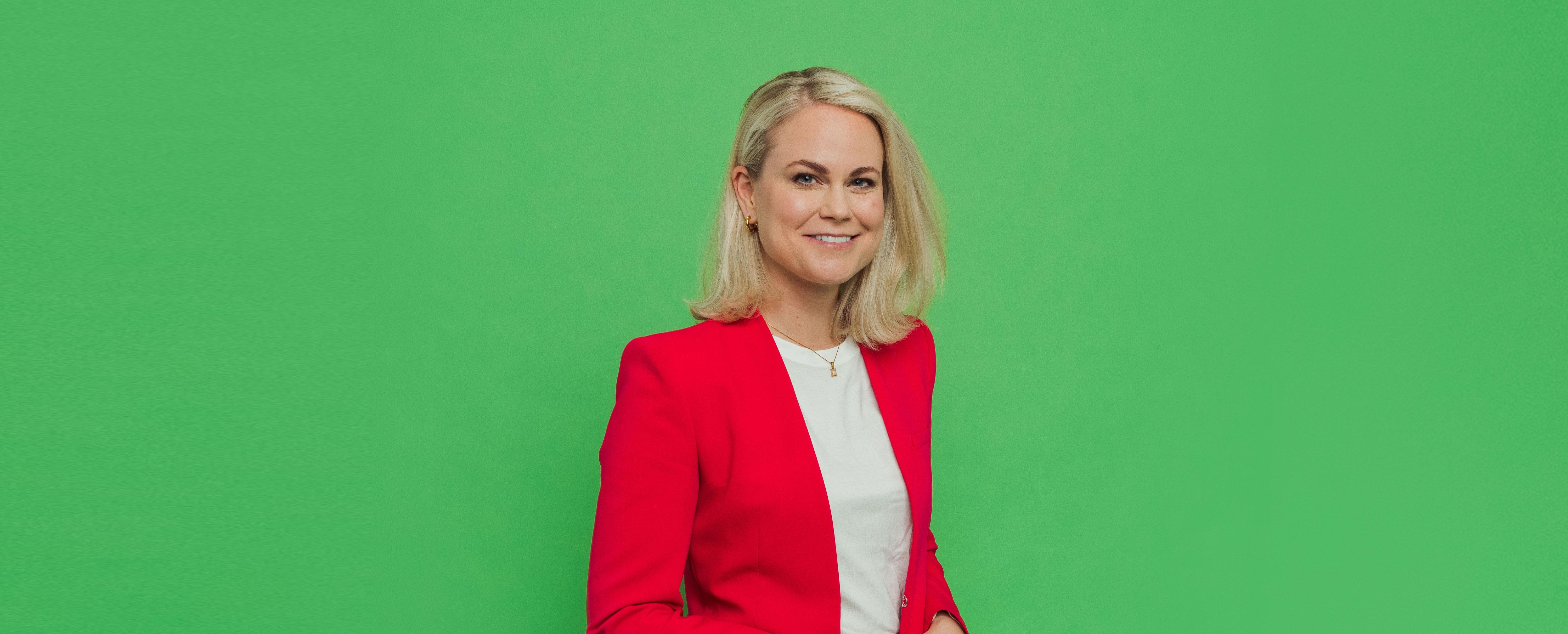 Porträttbild Camilla Bergman i röd kavaj mot grön bakgrund