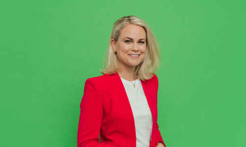 Porträttbild Camilla Bergman i röd kavaj mot grön bakgrund