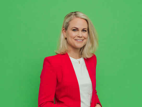 Porträttbild Camilla Bergman i röd kavaj mot grön bakgrund