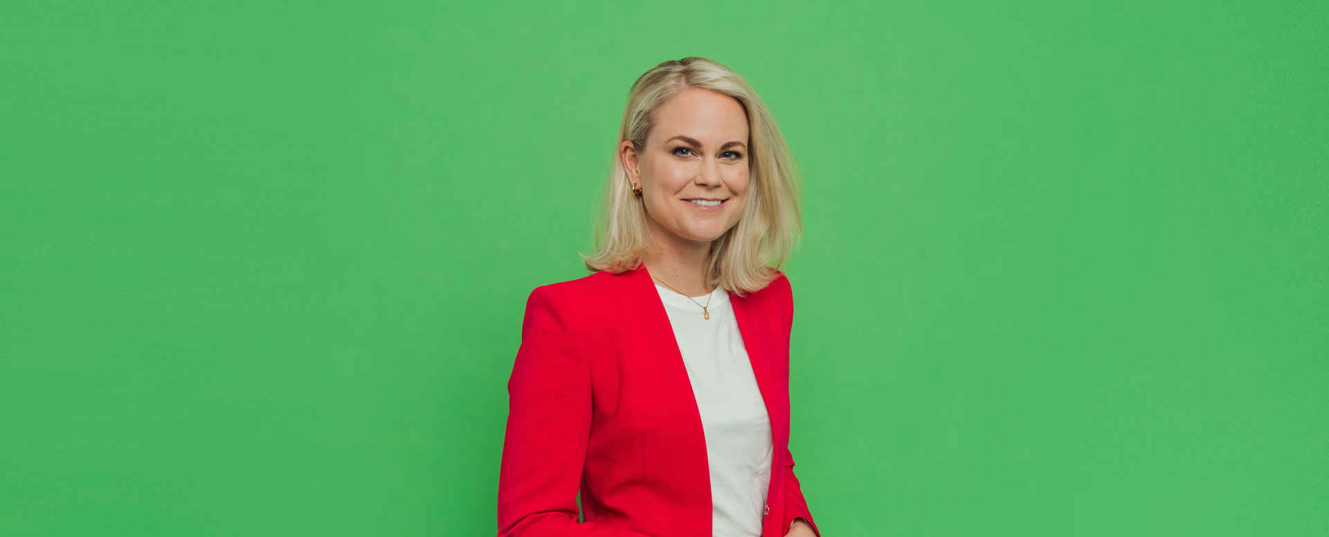 Porträttbild Camilla Bergman i röd kavaj mot grön bakgrund