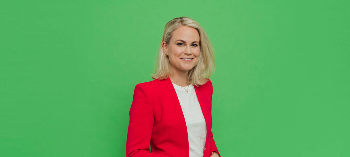Porträttbild Camilla Bergman i röd kavaj mot grön bakgrund
