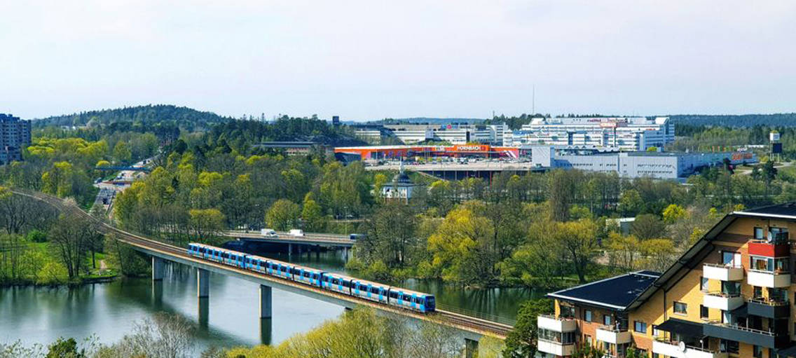 Landskapsvy som visar kontorsbyggnader, bostadshus och tåg på järnväg över vatten