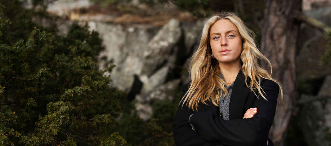 Kvinna med ljust hår och svart kavaj framför en skog