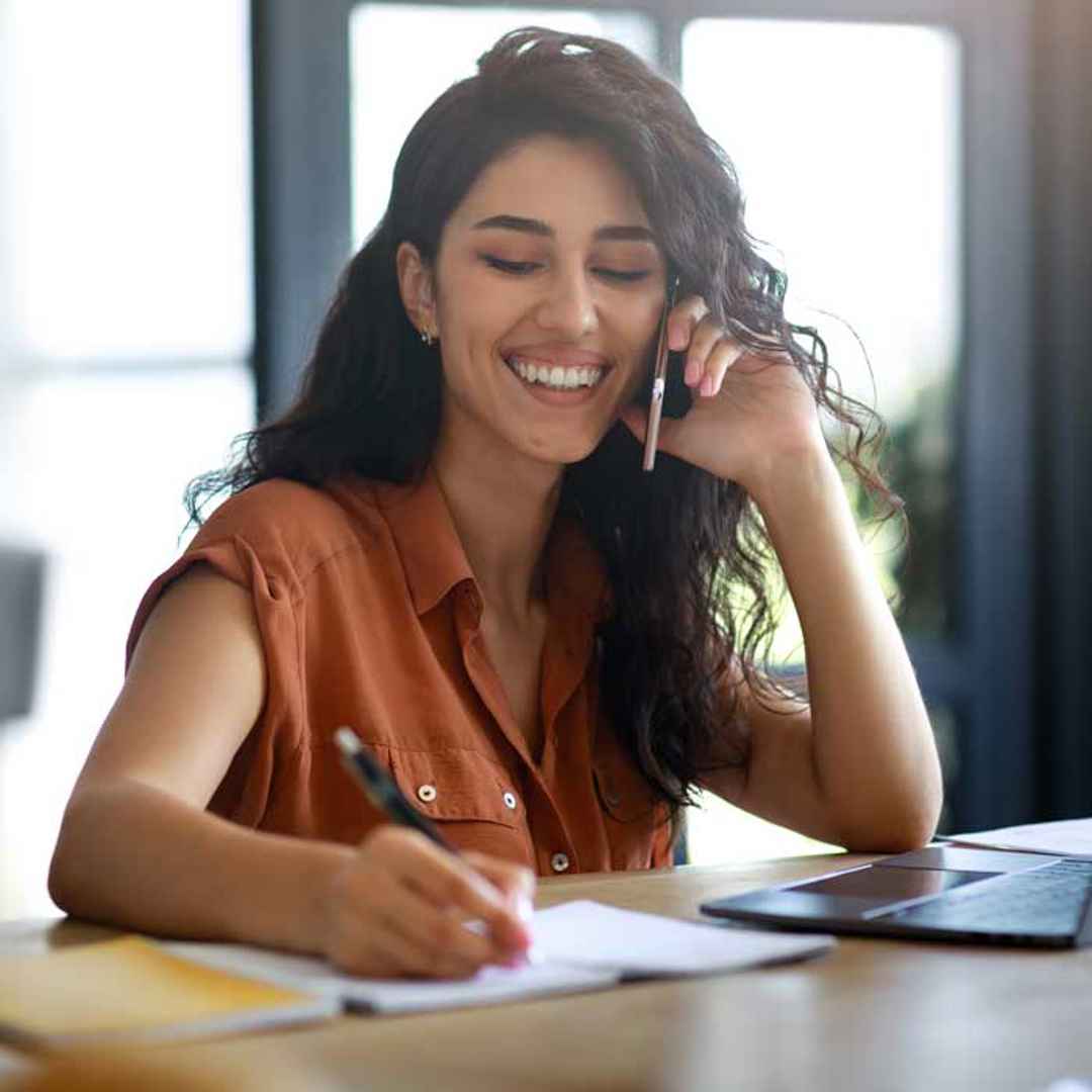 Kvinna pratar i telefon och skriver i ett dokument