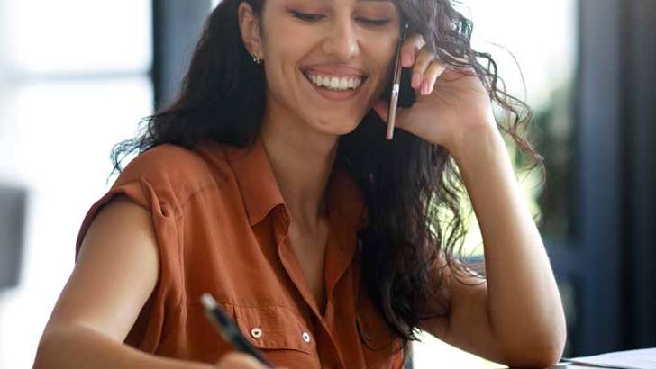 Kvinna pratar i telefon och skriver i ett dokument