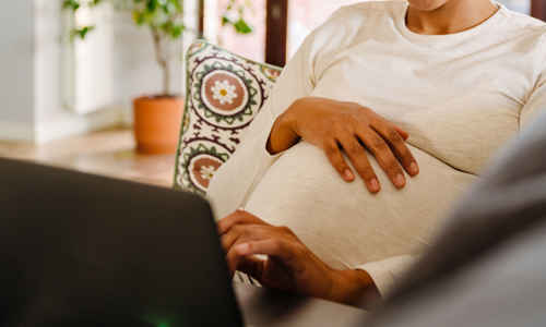Gravid kvinna med laptop i soffa