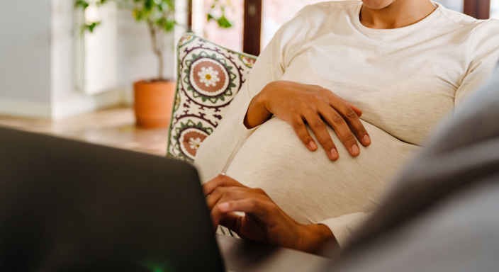 Gravid kvinna med laptop i soffa