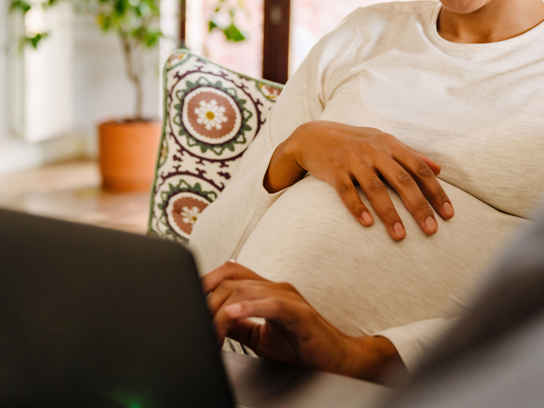 Gravid kvinna med laptop i soffa