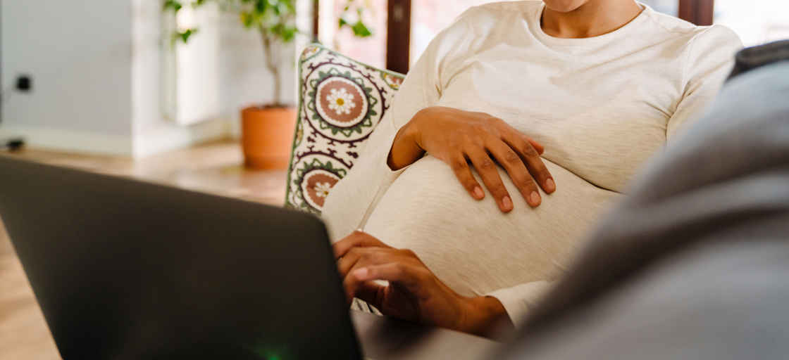 Gravid kvinna med laptop i soffa