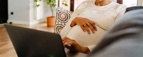 Gravid kvinna med laptop i soffa