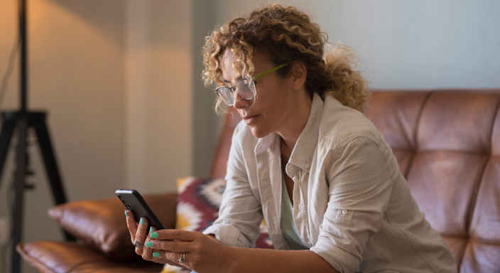 Kvinna med glasögon i soffa med mobil