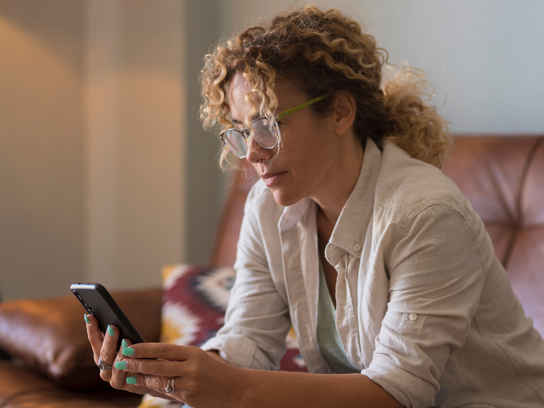 Kvinna med glasögon i soffa med mobil