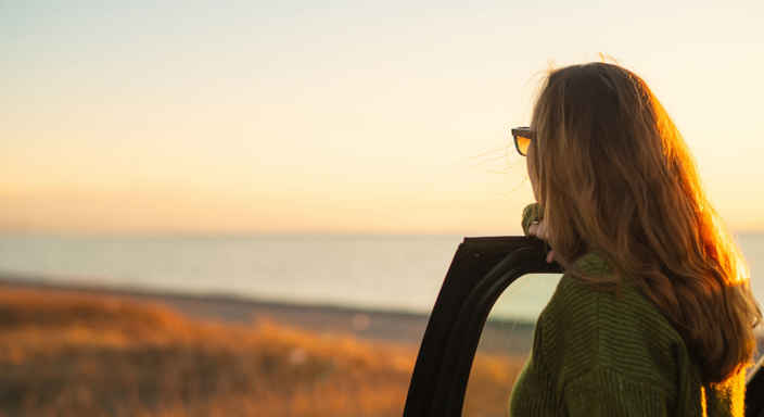 Kvinna vid öppen bildörr ser ut över havet