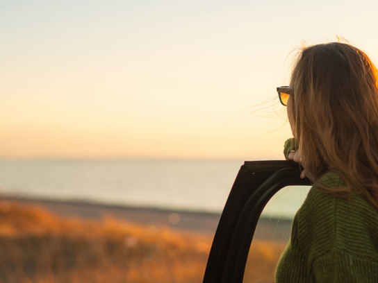 Kvinna vid öppen bildörr ser ut över havet