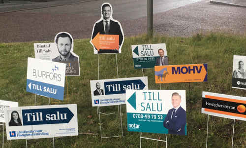 Till-salu-skyltar från mäklare i en gräsmatta