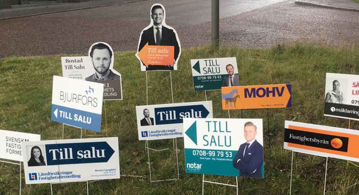 Till-salu-skyltar från mäklare i en gräsmatta