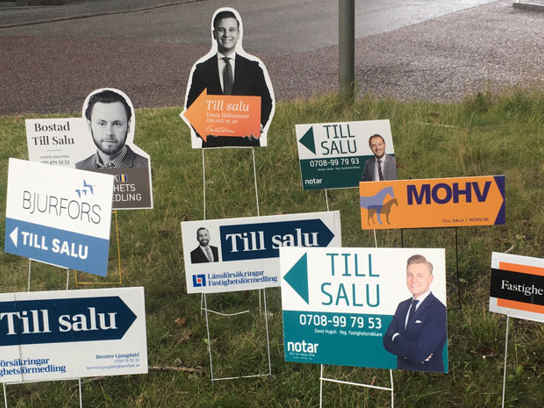 Till-salu-skyltar från mäklare i en gräsmatta