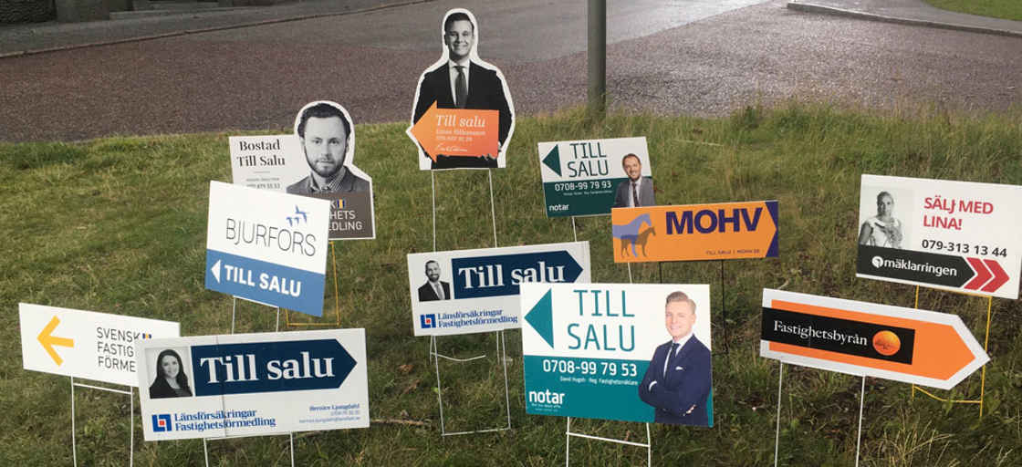 Till-salu-skyltar från mäklare i en gräsmatta