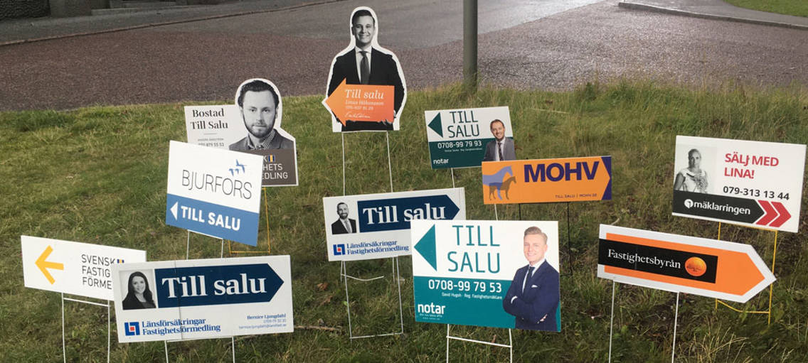Till-salu-skyltar från mäklare i en gräsmatta