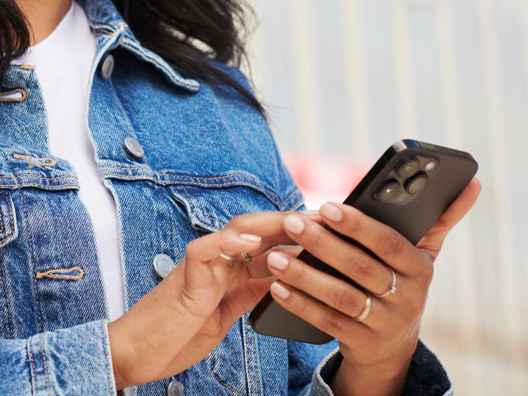 Kvinna i jeansjacka som knappar på sin mobiltelefon