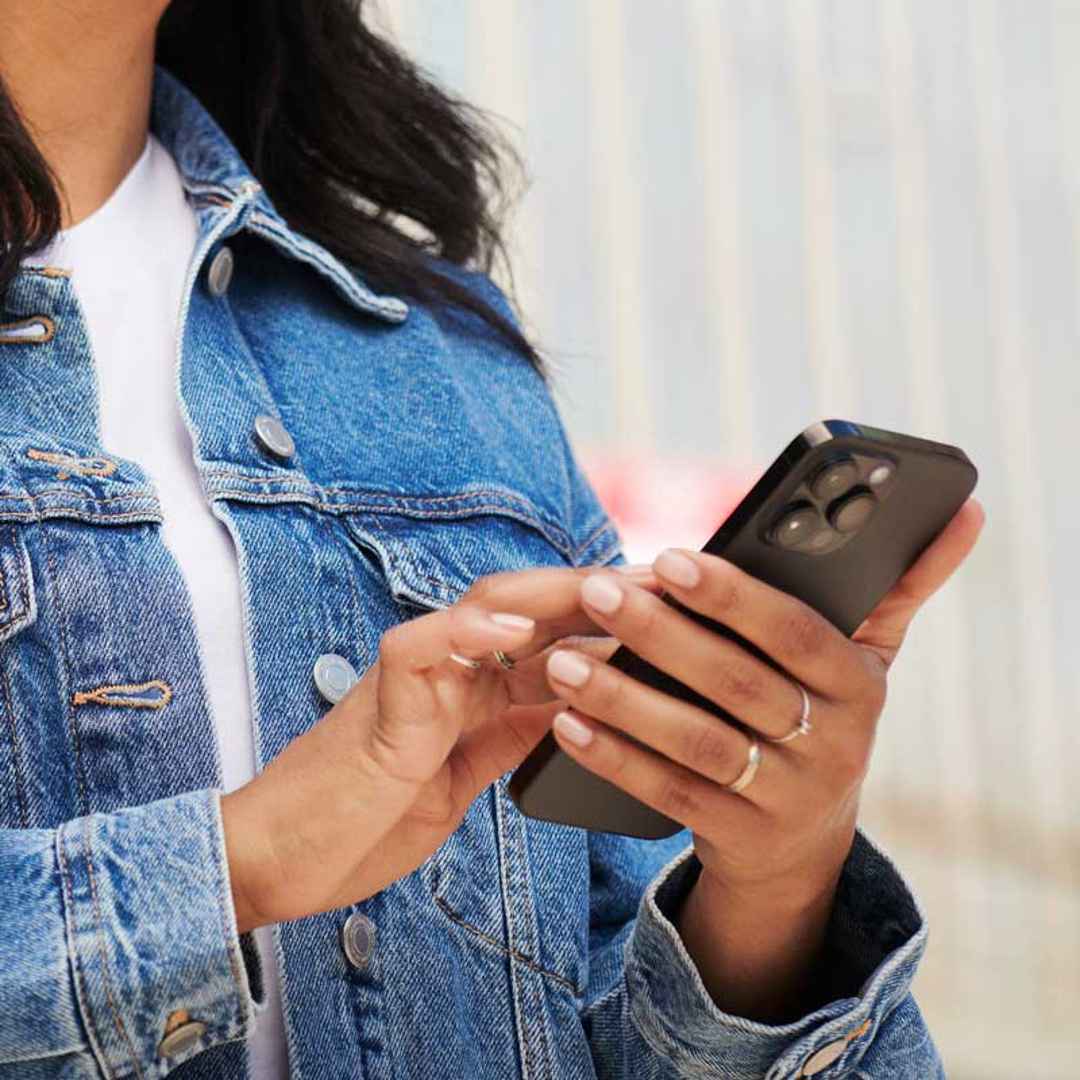 Kvinna i jeansjacka som knappar på sin mobiltelefon