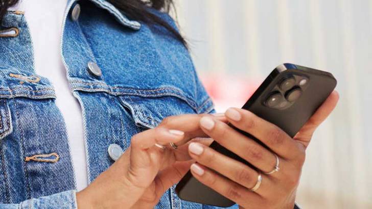 Kvinna i jeansjacka som knappar på sin mobiltelefon