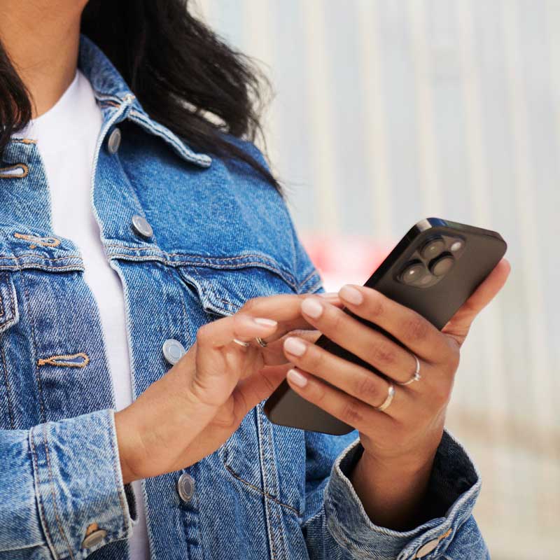 Kvinna i jeansjacka som knappar på sin mobiltelefon
