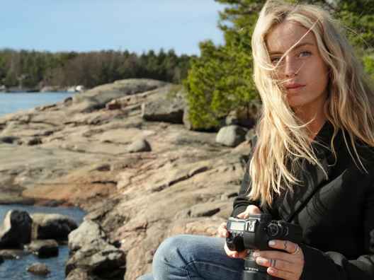Kvinna med ljust hår, sitter på en klippstrand
